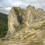 A large limestone rock formation on a grassy ridge above a forested valley